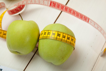 Green apples with measuring tape on a white wooden table