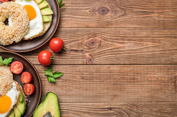 Bagel with avocado and egg on the wooden background.