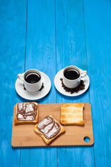 Two cups of coffee and toast with chocolate on a blue wooden table