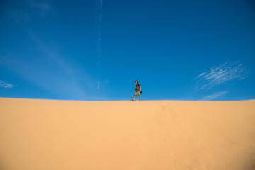 A man walking on white sand dune and blue sky in Mui Ne city, Vietnam