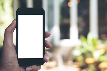 Mockup image of hand holding black mobile phone with blank white screen in loft cafe and green nature