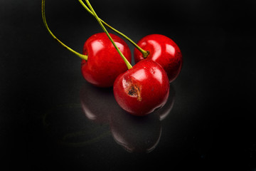 Two red cherries and one broken against reflective black background. Selective focus. Lights and shadows