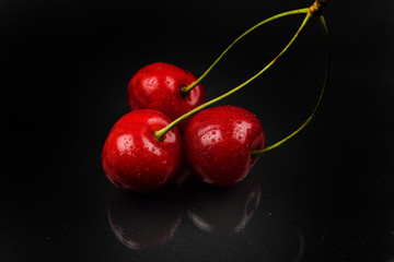 Three red cherries with water drops against reflective black background. Selective focus. Lights and shadows. Healthy and sweet food