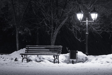 bench under winter trees and shining street lantern, falling snowflakes