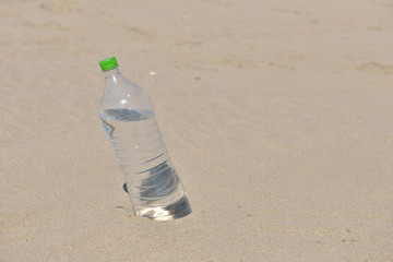 Ice cold unlabelled bottle of refreshing water standing upright in the golden sand on a tropical beach under the hot rays of the summer sun. Water requirements, heat