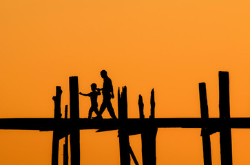 silhouette of father and son crossing the river on the longest bridge in the world, U-Bein bridge, Mandalay, Myanmar.