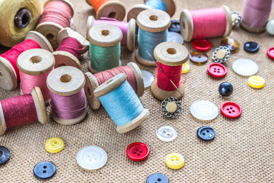 sewing tools (many different colorful thread, needle, many different buttons) on wooden background