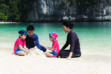 Fototapeta na wymiar Asian family with father, mother and daughter on beach making sand castles near sea. Summer Travel Vacation and Holiday concept.