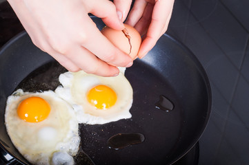 Woman's hands breaking breaking eggs into frying for Sunday's breakfast. Healthy eating concept
