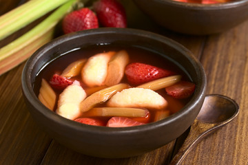 Warm or cold fruit soup made of strawberry, rhubarb and semolina dumplings served in rustic bowl, photographed on dark wood with natural light (Selective Focus, Focus one third into the soup)