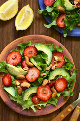 Strawberry, avocado, lettuce salad with cashew nuts on plate, photographed overhead on dark wood with natural light