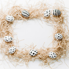 Frame of fancy Easter eggs in nest on white background. Flat lay, top view. Traditional spring concept.