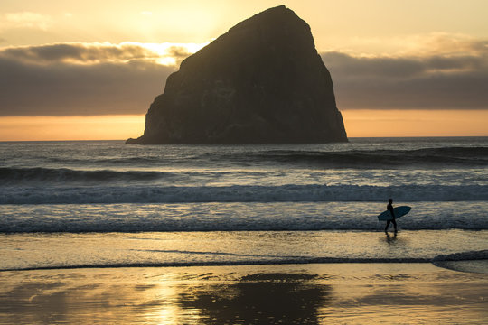 Man carrying surfboard while walking on beach at sunset 