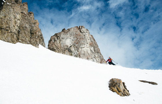 Skier descending snowy slope by rock formations 