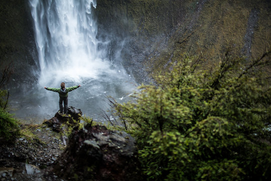 Person looking at waterfall with arms in air 