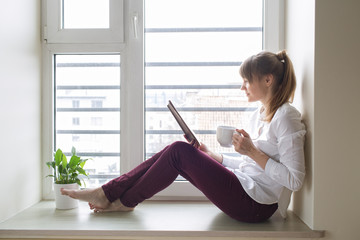 Woman reading a book and drinking coffee at the window