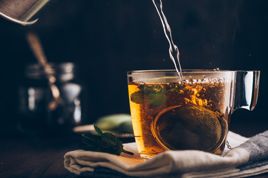 Pouring hot water into a cup of tea on dark background