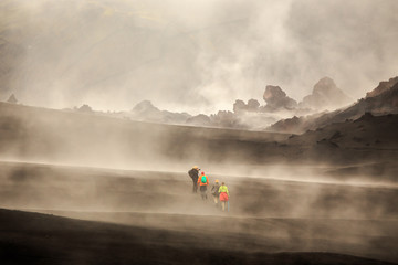 Tourists walking among  steaming lava fields with volcano slope in background