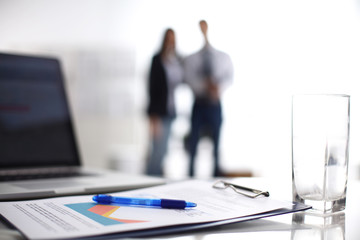 Laptop computer with folder on desk , two businesspeople standing in the background