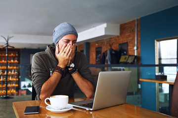 Worried shoked man with beard looking on laptop at cafe