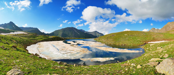 Mountain Lake with clean water and ice in the Caucasus summer. Blue sky with white clouds.
