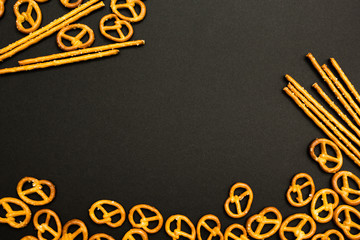Background texture of salted salty pretzels and mini sticks in the traditional form of the hinge assembly on a black background. Space for text.