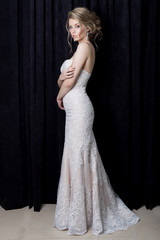 Fototapeta premium beautiful gentle girl sexy bride in a beautiful lace dress with a train with evening hairstyle and make-up in the studio on a black background