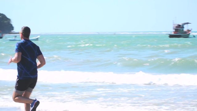 mann l&auml;uft mit laufschuhen und kurzer hose am strand von bang tao, phuket, thailand