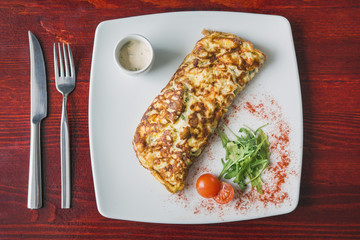 Top view of omelette with cherry tomato and greens on white plate, food background