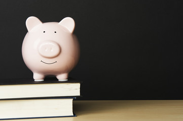 Piggybank on wooden table top, standing on top of a stack of books on a black background.