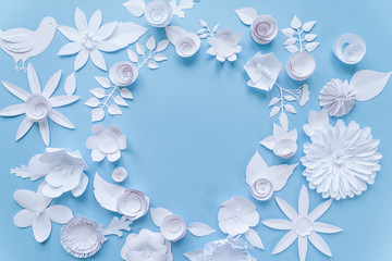 Round frame with white paper flowers on blue background. Cut from paper.