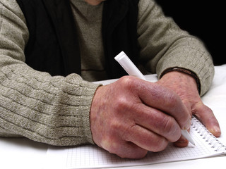 Closeup of the wrinkled hands of an old caucasian man holding pen and paper