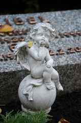 Fototapeta na wymiar kleine nette engelsfigur sitzt auf einem grab