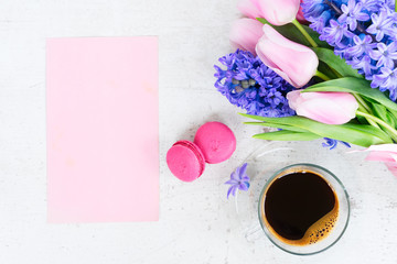 Pink tulips and blue hyacinths flowers with cup of coffee on white wooden table with copy space on pink paper card