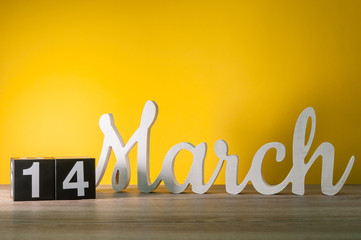 March 14th. Day 14 of month, daily wooden calendar on table with yellow background. Spring time....