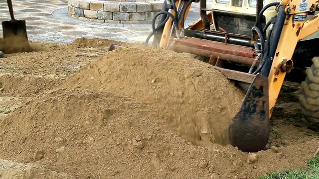 Front end loader moves a pile of dirt near a recently constructed backyard stone patio. 