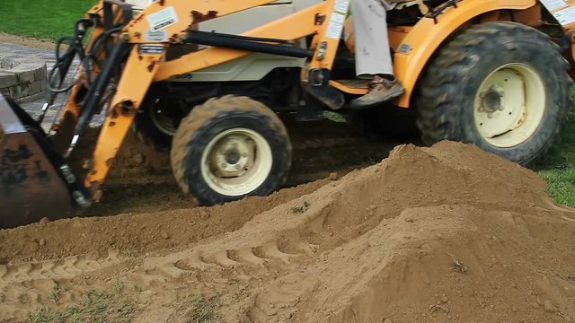 Front end loader moves a pile of dirt near a recently constructed backyard stone patio. 