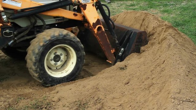 Front end loader moves a pile of dirt near a recently constructed backyard stone patio. 
