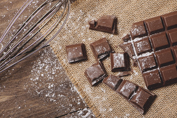 Tablet and chocolate pieces with icing sugar next to cookware. Horizontal shoot..