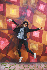 stylish young woman in hat jumping near the wall with graffiti 