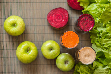 three glasses of different fresh juice. Beet, carrot and apple juices on grey wood background
