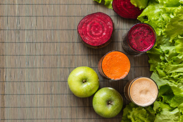 three glasses of different fresh juice. Beet, carrot and apple juices on grey wood background