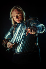 Powerful blond knight with the sword on the dark background