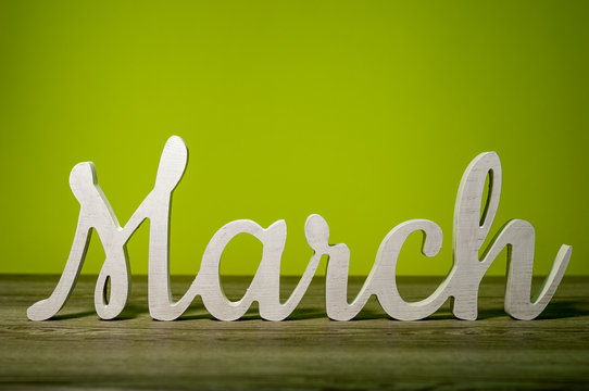 Close Up March word carved out of wood on green background. Spring beginning concept