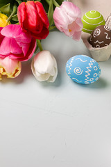 Fototapeta na wymiar Painted easter eggs and bouquet of spring tulips closeup on a light blue background with space for congratulation