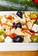 Simple, fresh salad with vegetables, olives and cheese in white bowl on a wooden board.