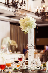 Restaurant decorated for wedding banquet. Original gigantic vase of beautiful white hydrangea stands in the middle covered festive table