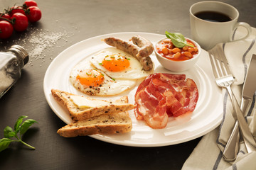 Full english breakfast on white plate, black background.
