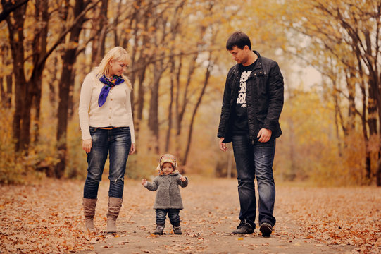 Молодые родители идут в осеннем парке со своим маленьким ребенком
