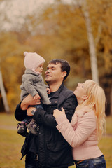 Fototapeta premium Молодые родители держат на руках маленькую дочь в осеннем парке